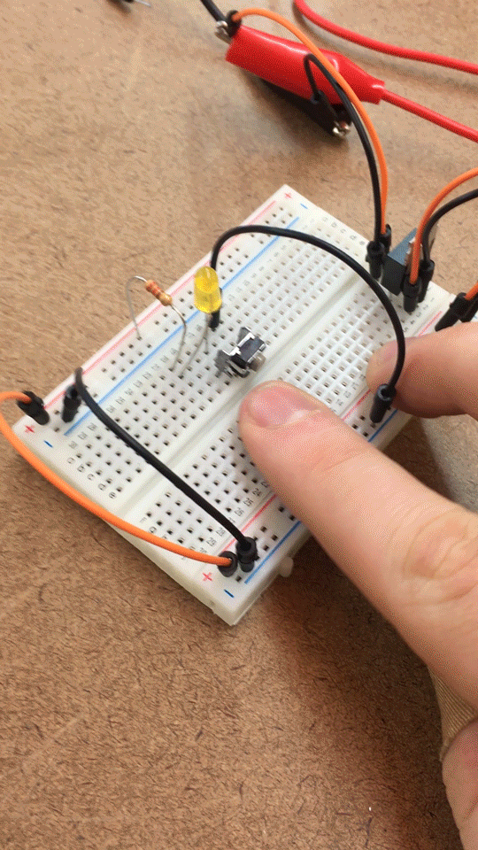 Finger pushing button on breadboard. When the button is pressed, a yellow LED turns on.