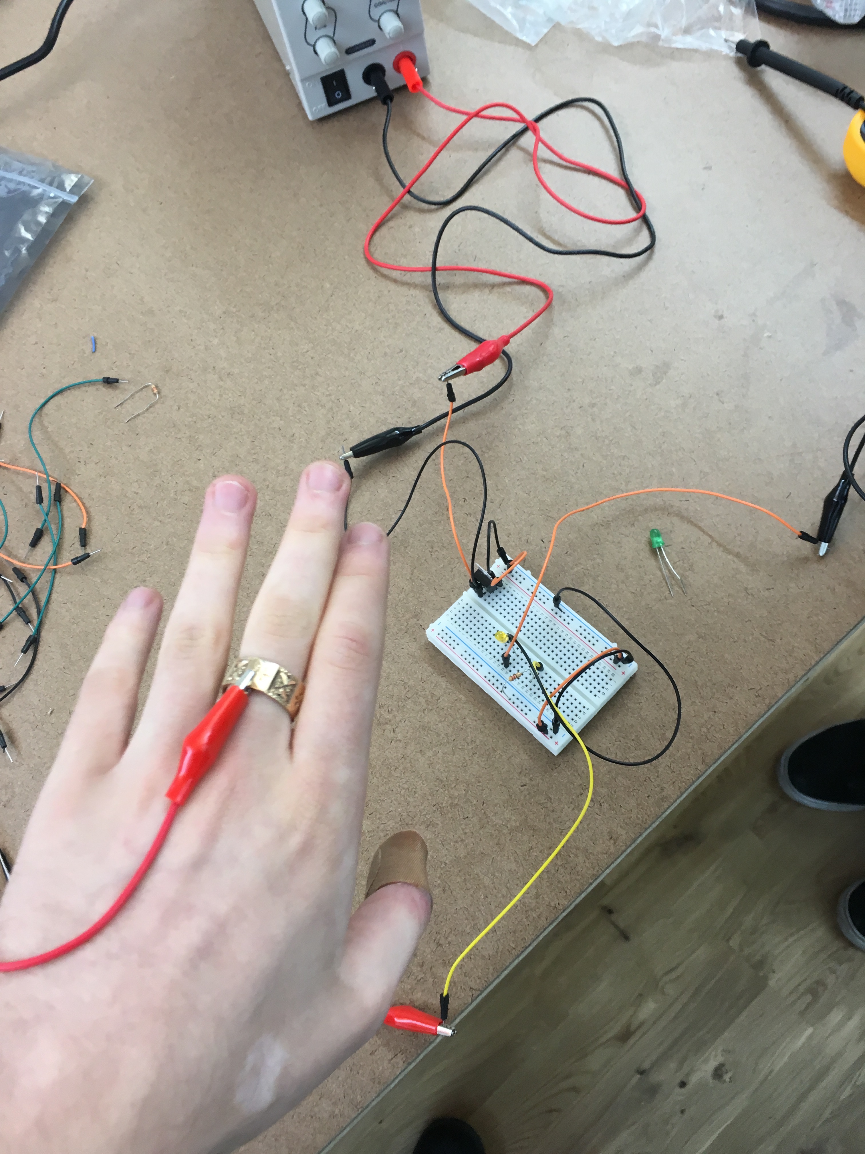 Foreground: Alligator clip connected to gold ring. Background: Breadboard setup for LED.